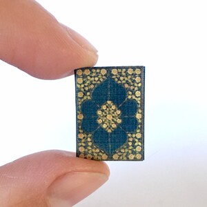 May include: A small, blue rug with a gold floral pattern. The rug is about the size of a hand.