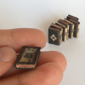 May include: A miniature book with a gold and black cover. The book is titled "The Tiger" and has a decorative design on the cover. The book is being held in a hand.