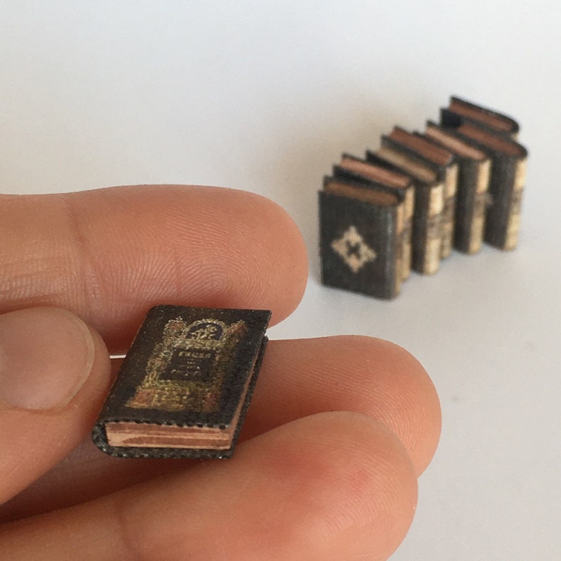May include: A miniature book with a gold and black cover. The book is titled "The Tiger" and has a decorative design on the cover. The book is being held in a hand.
