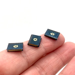May include: Three miniature books with black covers and gold accents. Each book has a small, gold design on the front cover.