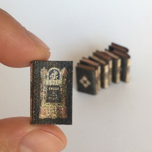 May include: A miniature book with a black cover and gold lettering. The book is titled "The Book of Common Prayer".