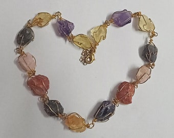 May include: A gold wire wrapped necklace with various colored gemstones. The necklace is shaped like a heart.