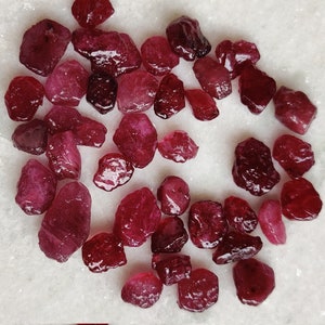 May include: A collection of loose, raw ruby gemstones in various sizes and shapes. The rubies are a deep red colour and have a natural, unpolished finish.