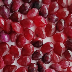 Op de afbeelding: Een verzameling rode edelsteenparels in peervorm. De parels zijn gefacetteerd en hebben een glanzende afwerking.