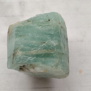 Pode incluir: Um grande cristal de &aacute;gua-marinha azul claro com uma textura &aacute;spera e natural. O cristal tem uma apar&ecirc;ncia ligeiramente nublada e &eacute; transl&uacute;cido.