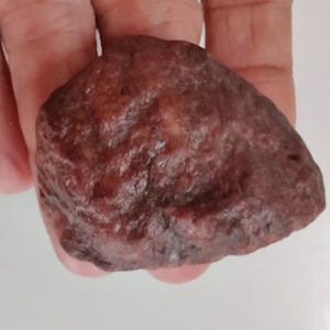 May include: A close-up of a dark red, irregularly shaped, smooth stone.