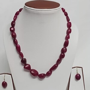 Op de afbeelding: Een set met een donkerrode edelsteen ketting en oorbellen. De ketting is gemaakt van gladde, ovale stenen en de oorbellen zijn eenvoudige oorbelletjes.