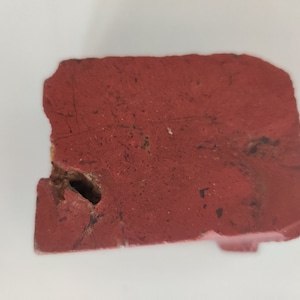 May include: A close-up of a red brick with a few scratches on the surface. The brick has a rough texture and a hole in the center.
