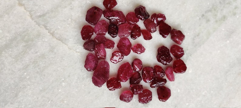 May include: A collection of loose, raw ruby gemstones in various sizes and shapes. The rubies are a deep red color and have a natural, unpolished finish.