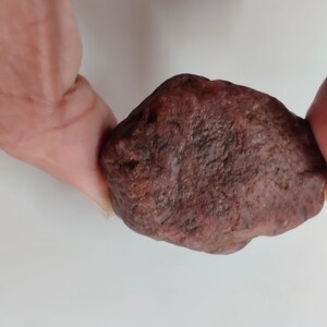 Könnte beinhalten: Ein großer, rauer, dunkelroter Edelstein. Der Edelstein ist unregelmäßig geformt und hat eine matte, stumpfe Oberfläche.