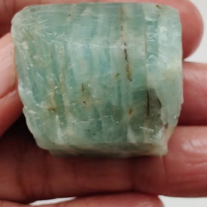 Pode incluir: Um cristal de &aacute;gua-marinha bruto, de cor verde claro, com estrias e inclus&otilde;es vis&iacute;veis.