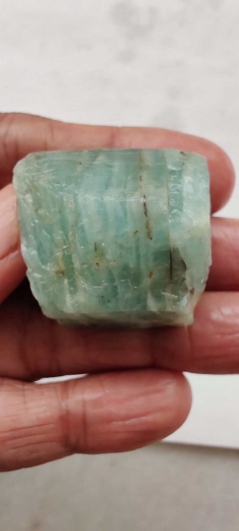 Pode incluir: Um cristal de &aacute;gua-marinha bruto, de cor verde claro, com estrias e inclus&otilde;es vis&iacute;veis.