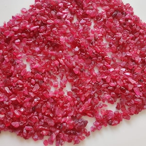 May include: A large pile of small, rough, red ruby gemstones. The rubies are various shapes and sizes.