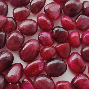 Può includere: Una collezione di pietre rotonde di gemme rosse, lisce e levigate. Le pietre sono di varie dimensioni e forme, con una finitura lucida.