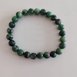 May include: A green gemstone bracelet with round beads. The beads have a mottled green and black pattern.
