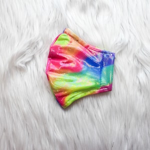 May include: A colorful tie-dye face mask with a glittery finish. The mask is made of a soft, stretchy fabric and has a rainbow pattern.