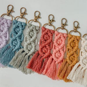 Puede incluir: Un conjunto de siete llaveros de macramé de colores con borlas. Los llaveros están hechos con hilo de diferentes colores y tienen un anillo de llave de metal dorado.