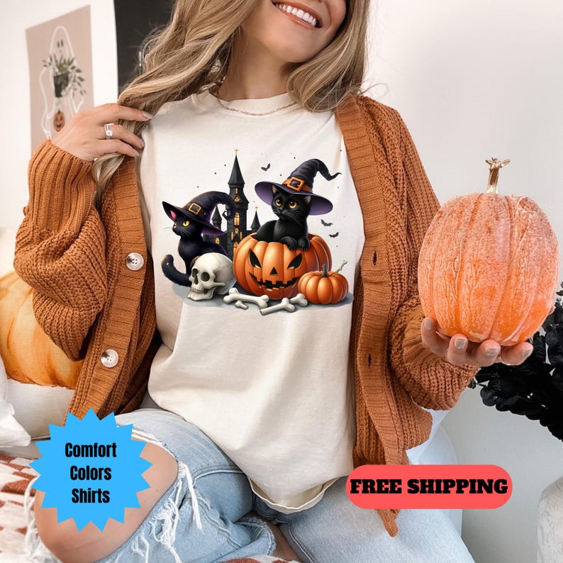 May include: White t-shirt with a black cat wearing a witch hat sitting inside a jack-o-lantern.  The cat is holding a small bat in its paw.  There is a second black cat wearing a witch hat and a skull next to the jack-o-lantern.  The text "FREE SHIPPING" is on the bottom right corner of the image.