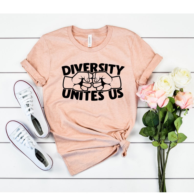 May include: A peach-colored t-shirt with the text "DIVERSITY UNITES US" in black, featuring two fists bumping. White canvas sneakers and a bouquet of pink and white roses are also in the image.