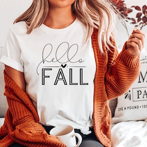 May include: A white t-shirt with the text "hello fall" in black lettering with a small heart between the words.