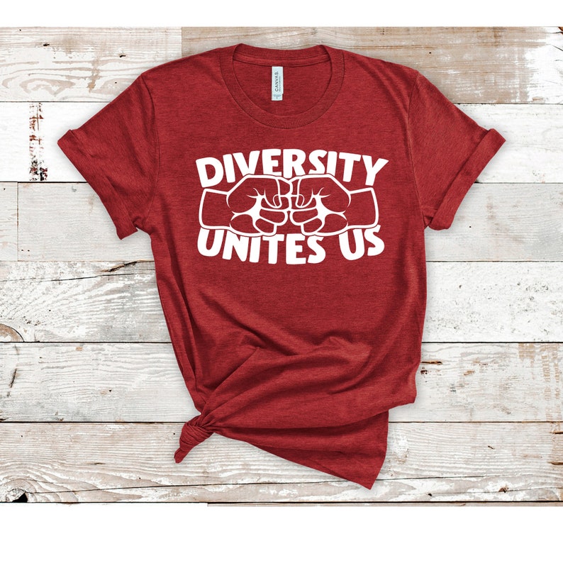 May include: A red t-shirt with the text "DIVERSITY UNITES US" in white block letters. The text is above two white fists bumping together. The shirt is knotted at the bottom and has rolled-up sleeves.