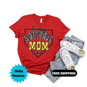 May include: Red t-shirt with a white and black leopard print softball design inside a red baseball diamond. The text "In my Softball Mom Era" is written in yellow and black.