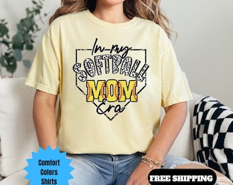 May include: A yellow t-shirt with a black and white softball graphic that says "In My Softball Mom Era".