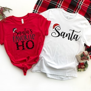 May include: Two red and white Christmas themed t-shirts. One shirt says "Santa's Favorite Ho" with a Santa hat graphic. The other shirt says "Santa" with a Santa hat graphic.