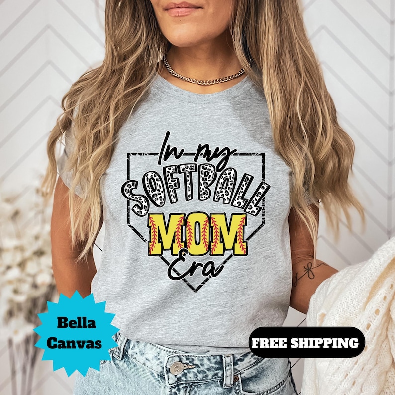 May include: Gray t-shirt with a black and white leopard print softball design. The text on the shirt reads "In my Softball Mom Era".