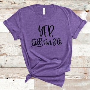 Op de afbeelding: Paars T-shirt met de tekst "Yep, still single" in zwarte letters.