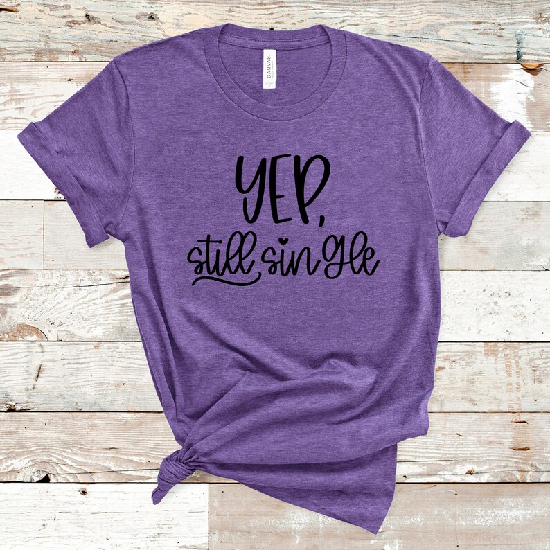 Op de afbeelding: Paars T-shirt met de tekst "Yep, still single" in zwarte letters.