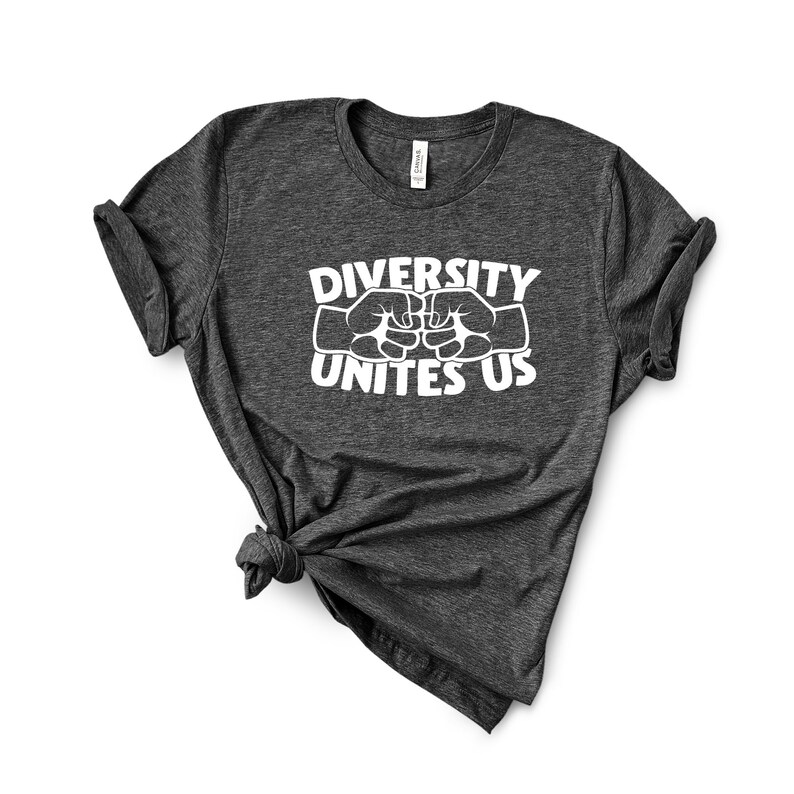 May include: Dark gray t-shirt with the text "DIVERSITY UNITES US" in white. The design features two fists bumping, symbolizing unity. The shirt is made of a soft material and has a classic crew neck.