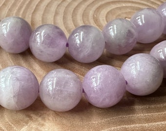 Peut inclure: Un collier de perles sphériques lisses de couleur lavande avec une finition polie. Les perles sont enfilées sur un cordon violet fin, mettant en valeur les variations naturelles de la texture de la pierre et des reflets brillants.