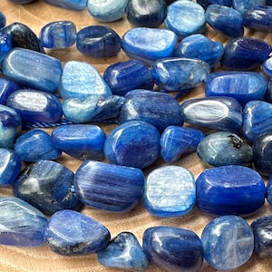 Pode incluir: Um fio de contas de pedra preciosa de cianita azul, polidas e polidas em formas ovais lisas. As contas têm um padrão estriado e uma variação de cor de azul claro a azul escuro.