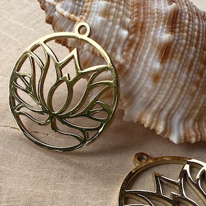 Könnte beinhalten: Zwei kreisförmige Anhänger aus goldfarbenem Metall mit einem ausgeschnittenen Lotusblumen-Design. Jeder Anhänger hat eine kleine Öse an der Oberseite zur Befestigung. Die Metalloberfläche ist glatt und reflektierend mit einem symmetrischen Blumenmuster.
