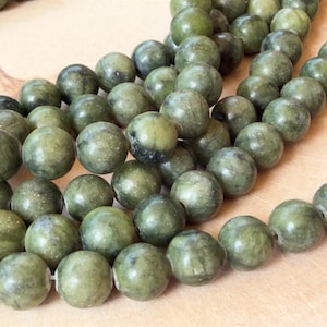 May include: A collection of round, smooth beads in varying shades of olive and forest green. Each bead features a polished surface with natural mottled patterns and subtle dark inclusions, strung together in multiple loose, overlapping strands.