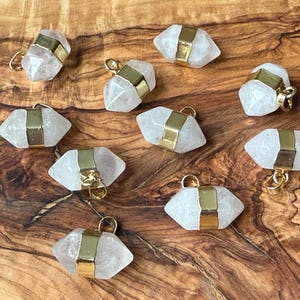 Pode incluir: Dez pingentes de cristal branco em forma de ponta com detalhes dourados. Os pingentes têm a forma de uma ponta e uma banda dourada em torno do centro. Os pingentes estão todos sobre uma superfície de madeira.