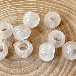Könnte beinhalten: Eine Ansammlung von neun durchscheinenden, cremeweißen, kugelförmigen Perlen mit einer glatten, polierten Oberfläche. Jede Perle hat ein zentrales Loch zum Auffädeln und zeigt eine subtile, wolkige Innenstruktur, die das Licht reflektiert.