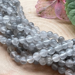 Könnte beinhalten: Eine Strähne runder, durchscheinender grauer Edelsteinperlen. Die Perlen sind glatt und haben eine leicht trübe Optik.