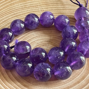 Könnte beinhalten: Eine Kette aus violetten Amethystperlen, jede Perle ist rund und glatt. Die Perlen sind auf einem dünnen violetten Faden aufgefädelt.