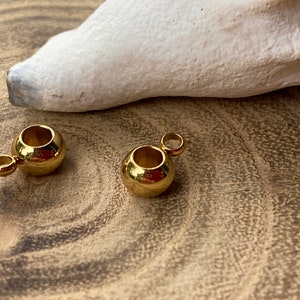 May include: Two gold-toned metal bead caps with a small loop on each. The bead caps are on a wooden surface.