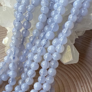 May include: A strand of light blue agate beads. The beads are round and smooth, and they have a slightly translucent appearance. The beads are strung on a clear thread.