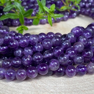 Könnte beinhalten: Eine Strähne runder, violetter Amethystperlen. Die Perlen sind glatt und poliert, mit einem leichten Glanz.