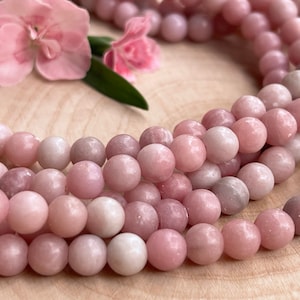 Könnte beinhalten: Eine Strähne rosafarbener Edelsteinperlen mit glatter, polierter Oberfläche. Die Perlen sind rund und gleichmäßig in der Größe und haben eine zarte, pastellrosa Farbe.