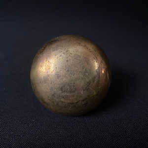 May include: A round, gold-colored metal object with a textured surface. The object is slightly dented and has a worn appearance.