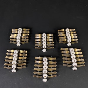 May include: Six sets of decorative drawer pulls with a brass finish and white ceramic knobs. Each pull has seven curved bars with a white knob on each bar.
