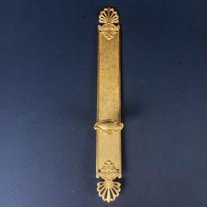 May include: A gold-toned door handle with ornate details and a decorative plate. The handle is designed to be used with a sliding door.