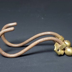 May include: A rusty metal double hook with two brass ball finials. The hook is curved and has a decorative brass plate.