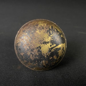 May include: A round, black and gold metal ornament with a distressed finish. The ornament has a textured surface and a worn look.
