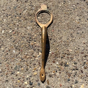 May include: A gold-colored metal door handle with a circular opening and a long, pointed handle.
